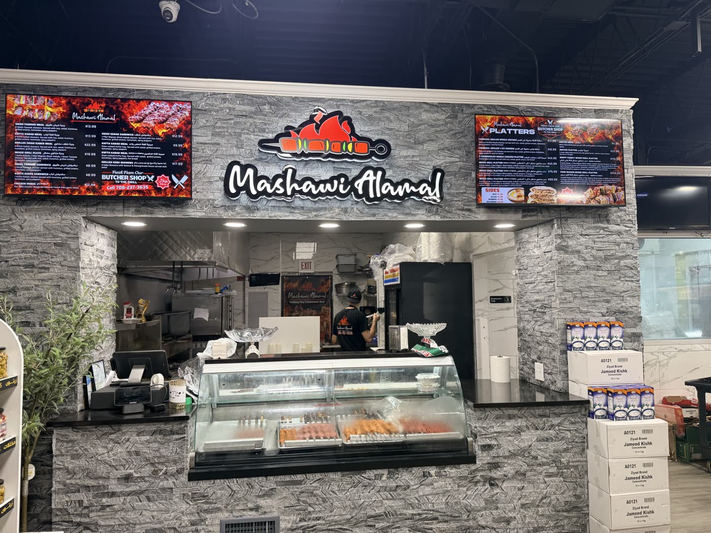 The Mashawi Alamal counter inside Al Amal Supermarket — the charcoal grill and menu boards straight ahead